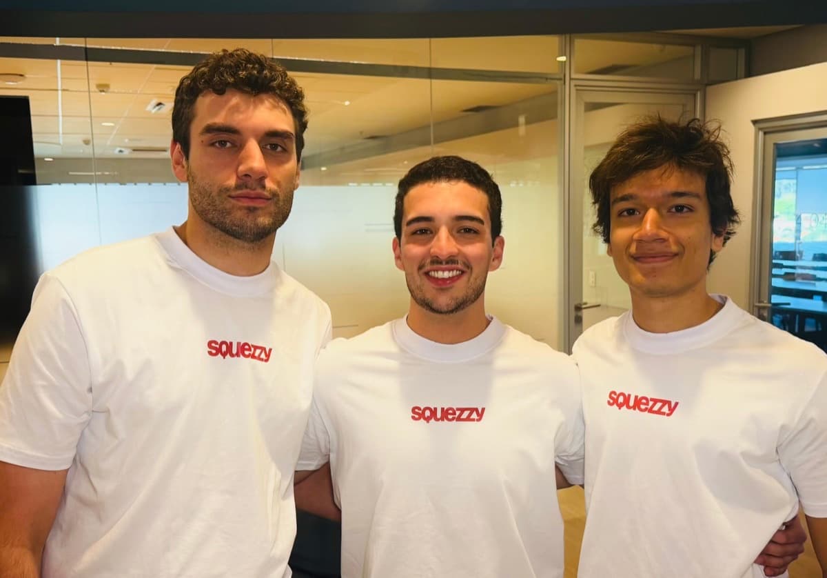 Gibran, Bruno e Luiz, os três fundadores da Squezzy, lado a lado num escritório, de camiseta branca com o logotipo da marca em vermelho.